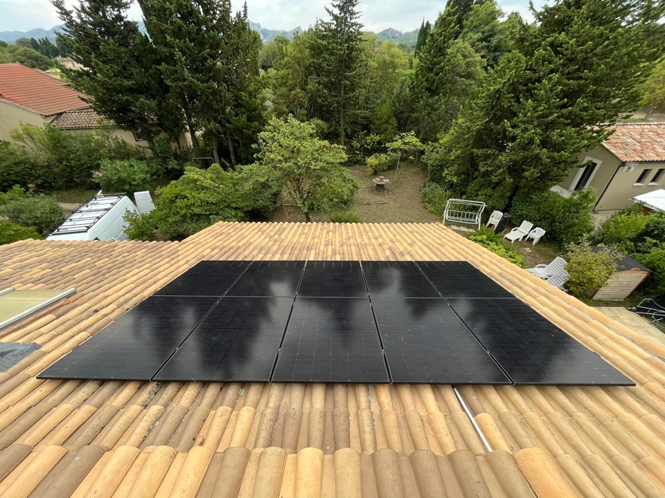 Installation de dix panneaux photovoltaïques noirs sur le toit en tuiles d'une maison avec jardin arboré