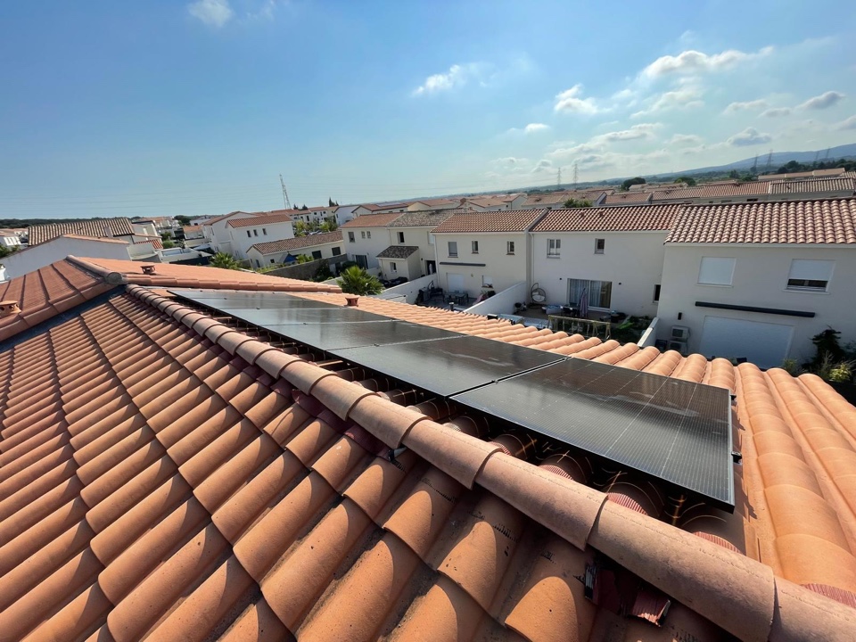 Panneaux photovoltaïques noirs alignés sous le faîtage d'un toit en tuiles, lotissement de maisons récentes