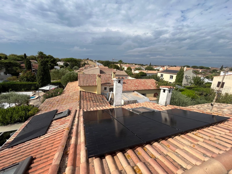 Panneaux photovoltaïques noirs posés sur un toit en tuiles canal dominant un quartier résidentiel arboré