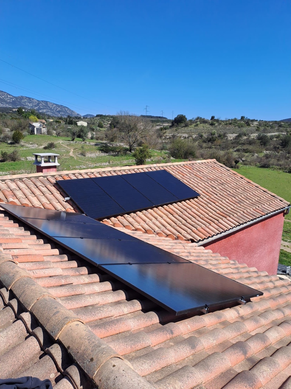 Deux groupes de panneaux photovoltaïques noirs en surimposition sur toit en tuiles canal, collines en arrière-plan