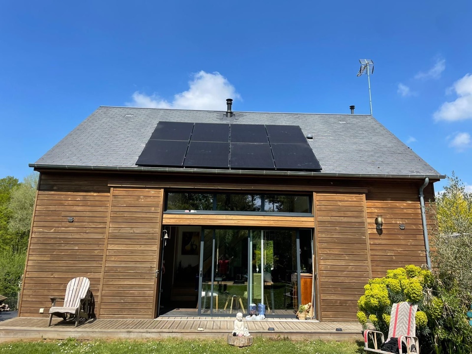 Huit panneaux photovoltaïques noirs sur le toit en ardoises d'une maison contemporaine en bois