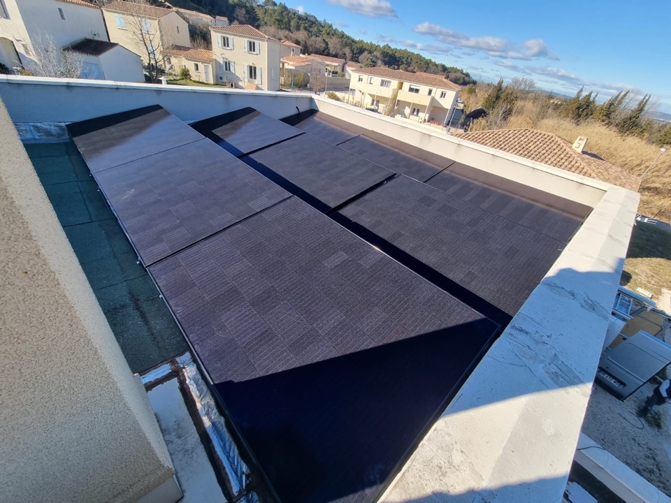 Panneaux photovoltaïques noirs installés sur un toit-terrasse avec vue sur un lotissement de villas