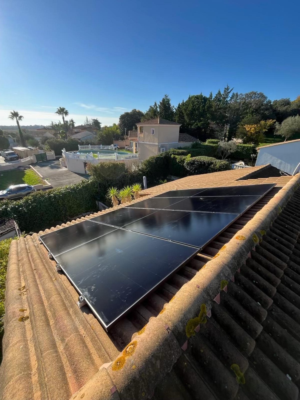 Panneaux photovoltaïques noirs sur un toit en tuiles canal, palmiers et villas en contrebas