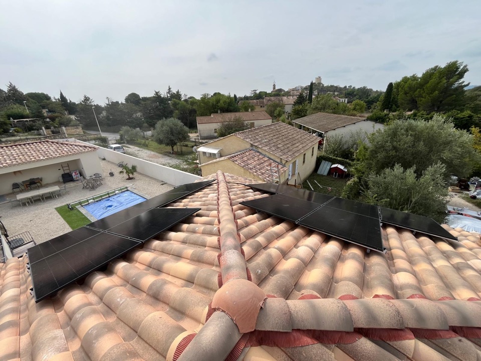 Panneaux photovoltaïques noirs posés sur un toit en tuiles canal, vue sur piscine et village
