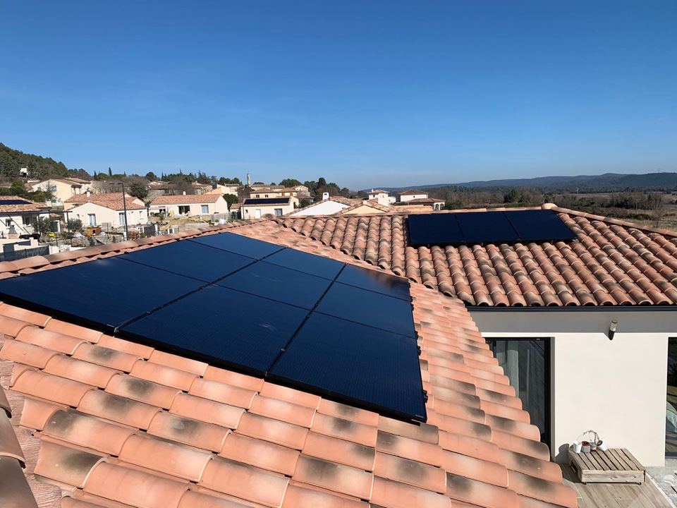 Panneaux photovoltaïques noirs installés sur le toit en tuiles d'une villa moderne, village en arrière-plan