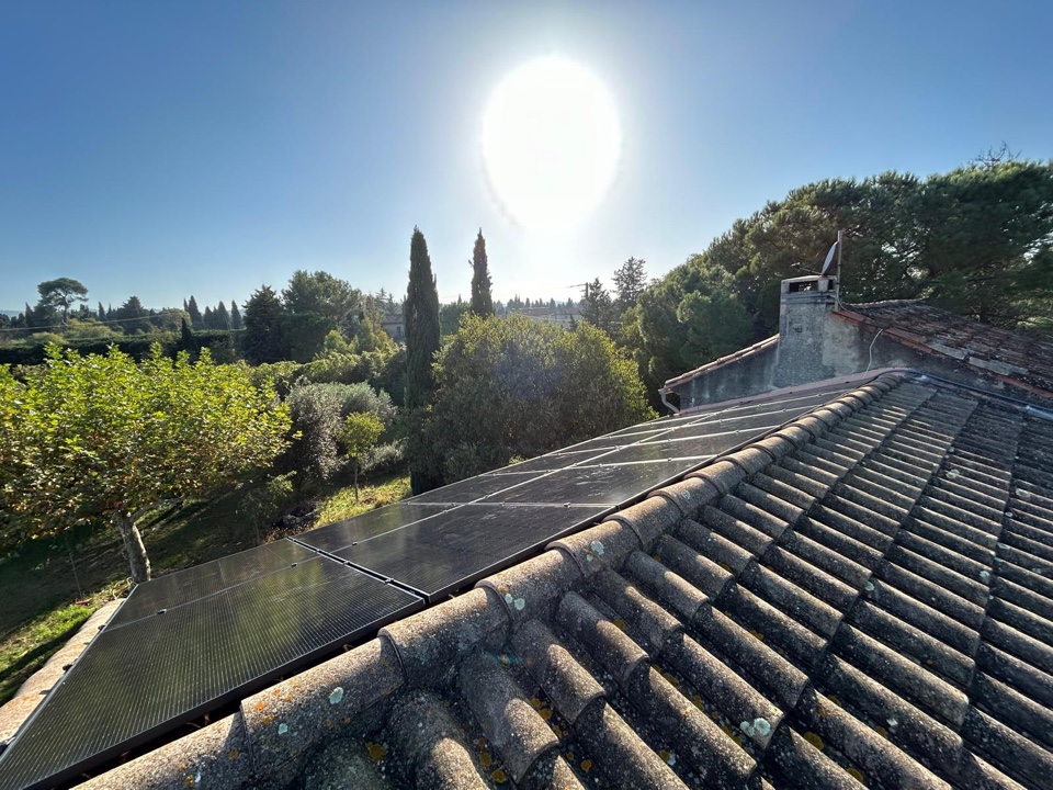Panneaux photovoltaïques sur un toit en tuiles au soleil, cyprès et pins en arrière-plan